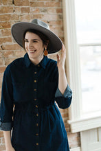 Woman wearing midi length dark denim dress with long sleeves that are rolled and button front closer detail front.