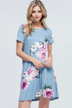 Woman wearing light blue mini soft material dress with purple floral pattern and bow tie back detail front.