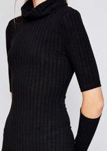 Woman in black knee length ribbed dress with cut out style at elbows and crowl neckline side.