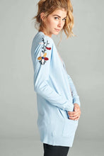 Woman wearing sky blue hip length long sleeve cardigan side.