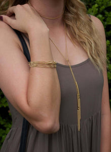 Woman wearing gold chain and tassel wrap around necklace.