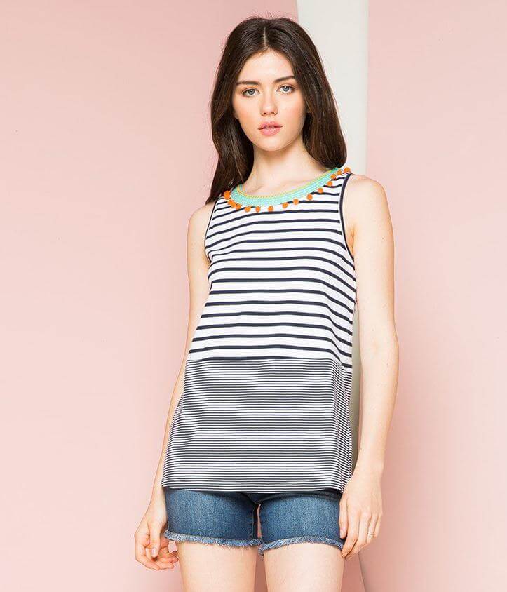 Woman wearing THML black and white stripped tank top with green embroidered neckline with orange ball details front.