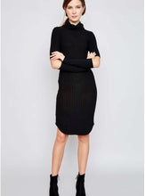 Woman in black knee length ribbed dress with cut out style at elbows and crowl neckline front.