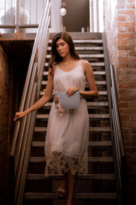 Woman walking down stair in elegant blue and white stripped slip dressed with lace hemline detail holding purse front..
