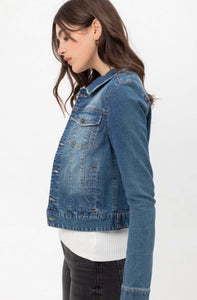 Woman wearing long sleeve button up front closure waist length blue jean denim jacket side.
