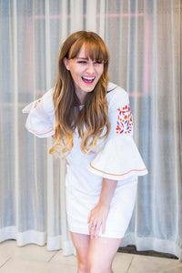Woman laughing and smiling wearing white mini dress with embroidered floral flare bell sleeves front.