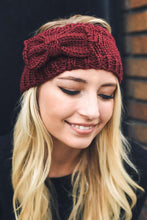 Blond woman wearing dark red knitted headband with bow.