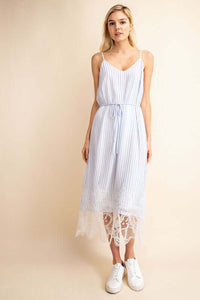 Woman in elegant blue and white stripped slip dressed with lace hemline detail holding purse front.