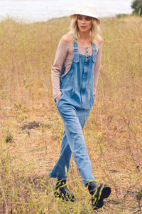 woman walking in grass field wearing wide leg baggy denim overalls 90s style.