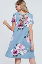Woman wearing light blue mini soft material dress with purple floral pattern and bow tie back detail back.