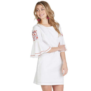 Woman smiling wearing white mini dress with embroidered floral flare bell sleeves front.