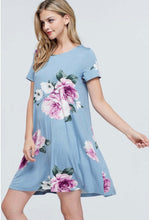 Woman wearing light blue mini soft material dress with purple floral pattern and bow tie back detail front.