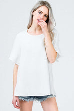 Woman in black loose fit white dress top blouse with ruffle mid length bell sleeves front.