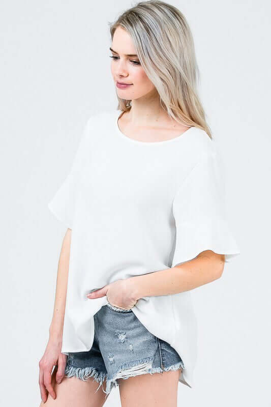 Woman in black loose fit white dress top blouse with ruffle mid length bell sleeves side.